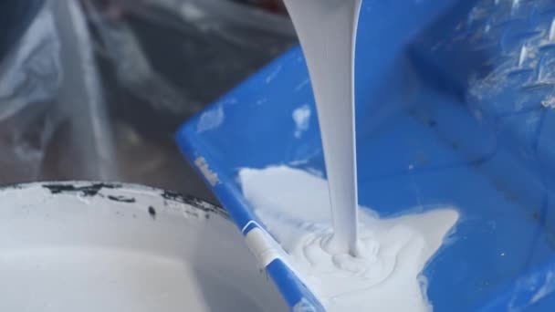 Worker painter pouring paint in a tray for painting walls using wooden spatula. — Stock Video