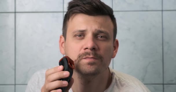 Jovem está barbeando barba e bigode usando lâmina elétrica, vista frontal. — Vídeo de Stock