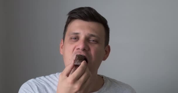 Człowiek je małe ciasto czekoladowe myszy patrząc t aparat, ciesząc się jego deser. — Wideo stockowe