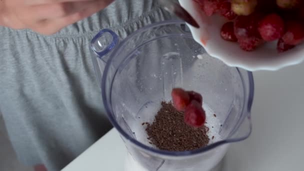 La mujer está cocinando batidos poniendo fresas congeladas en la taza de la licuadora, primer plano. — Vídeo de stock