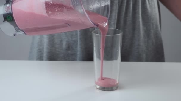 Woman is pouring strawberry smoothies in glass from blender cup, closeup view. — Stock Video