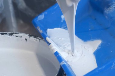 İşçi ressam, ahşap spatula kullanarak duvarları boyamak için tepsiye boya döküyor..