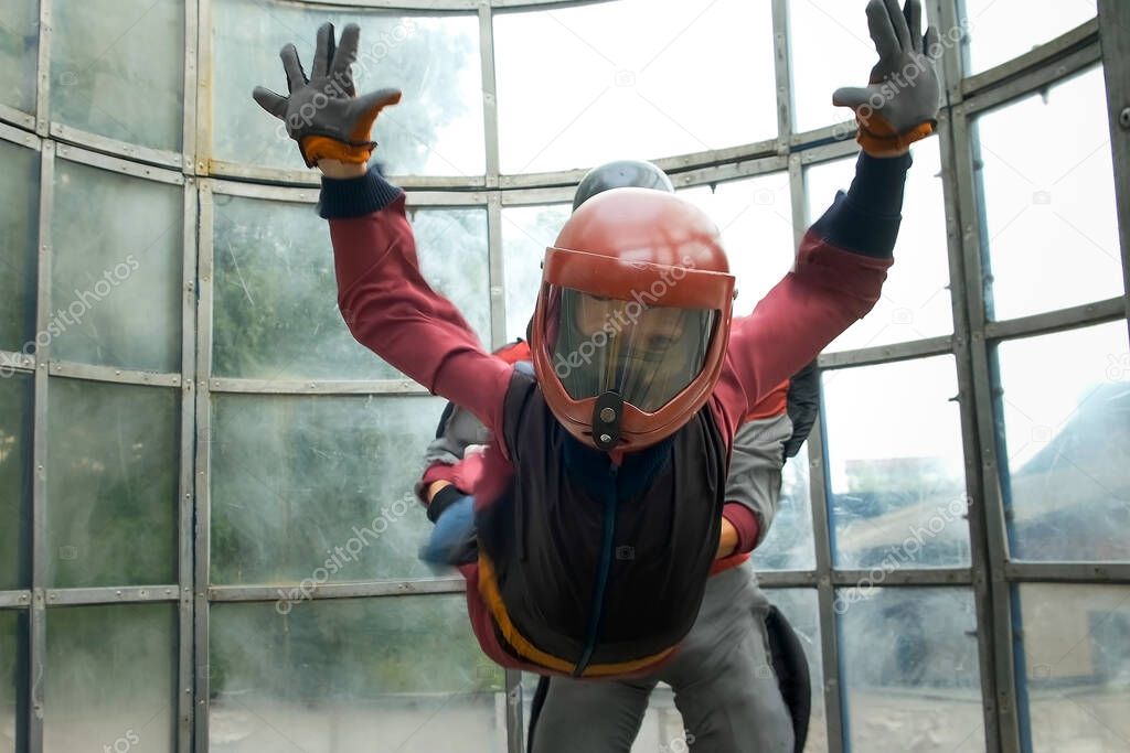 Child boy with instructor is flying in aerodynamic tube and looking at camera.