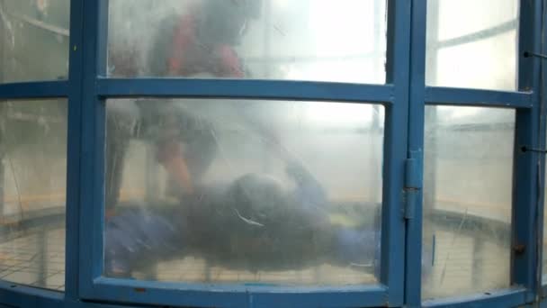 L'homme avec instructeur vole dans un tube aérodynamique, vue de l'extérieur. — Video