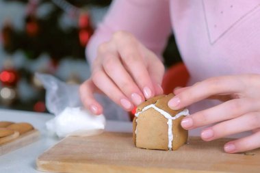 Kadın zencefilli kurabiye yapıyor. Parçaları şekerli kremayla yapıştırıyor. Elleri yakın plan..