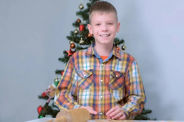 Pojken gör pepparkakor skära deg på julgran bakgrund. — Stockfoto