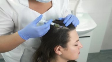 Doktor trikoloğu saç büyümesi için kadın derisine iğne yapıyor..