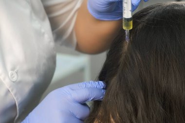 Doktor trikoloğu saç büyümesi için kadın derisine iğne yapıyor..