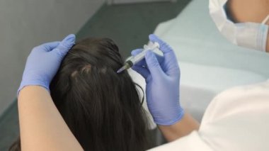 Doktor trikoloğu saç büyümesi için kadın derisine iğne yapıyor..