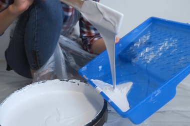 Kadın ressam, ahşap spatula kullanarak duvarları boyamak için tepsiye boya döküyor..