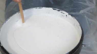 Bir galon gri boyayı ahşap boya karıştıran kadın elleri..