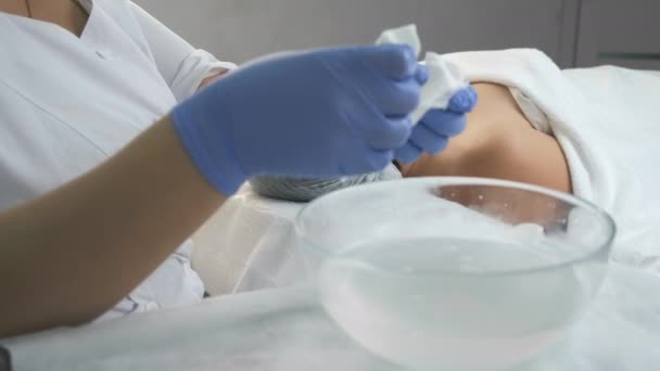 Dokter kosmetologi menyeka wajah wanita menggunakan serbet setelah prosedur mengupas. — Stok Video
