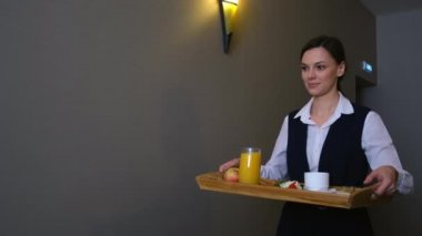 Kadın otel çalışanı hizmetçisi misafir odasına kahvaltı tepsisi taşıyor..