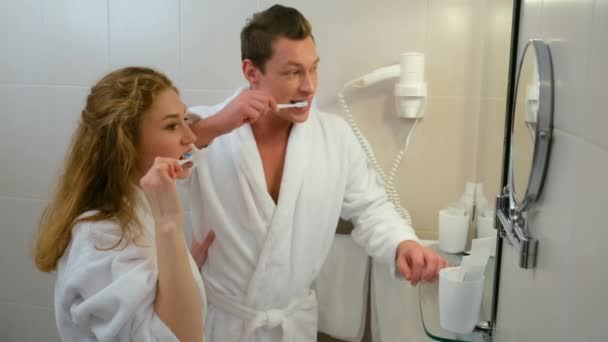 Bornozlu kadın ve erkek aynanın önünde dişlerini birlikte temizliyorlar.. — Stok video