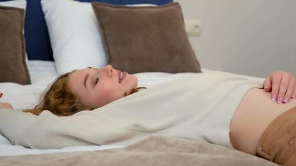Egy fáradt, boldog fiatal nő portréja fekszik az ágyon a hotelben, nehéz út után.. — Stock videók