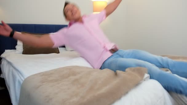 Mann og kvinne faller på senga på hotellrommet og klemmer sammen.. – stockvideo