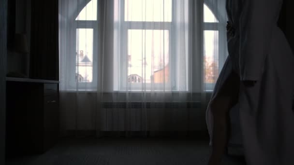 Силует молодої жінки в готелі біля вікна вранці, вид ззаду . — стокове відео