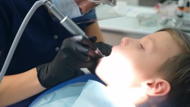 Dentysta higienista podejmowania higieniczne sprzątanie jamy ustnej w stomatologii dla nastolatka chłopiec. — Wideo stockowe