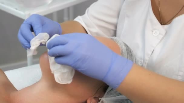 Cosmetologist is wiping womans face using napkins before peeling procedure. — Stock Video