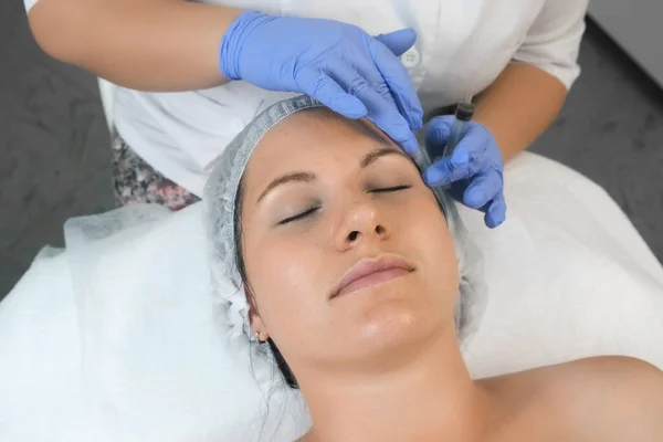Cosmetoloog brengt gele peeling op vrouwen gezicht in schoonheidskliniek. — Stockfoto