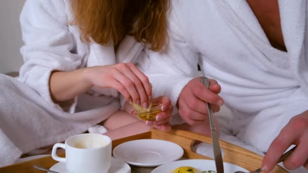 Jong stel in badjassen ontbijten samen op bed in hotelkamer. — Stockvideo