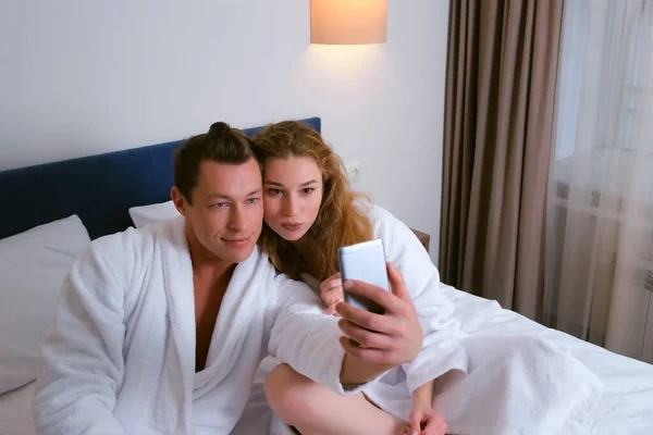 男性と女性でバスローブを着てホテルで食べるスマートフォンで写真を撮る. — ストック写真
