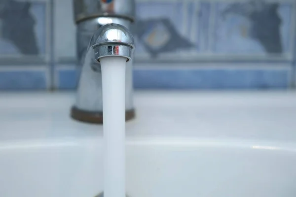 Чистая вода льется из блестящего крана в раковину в ванной комнате, крупным планом. — стоковое фото