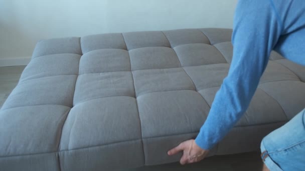 Hombre pliega el sofá moderno de color gris en la habitación, vista de cerca. — Vídeo de stock