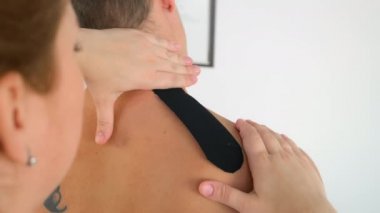 Fizyoterapist Kinesio bandını klinikte boyun omuzlarına yapıştırdı..