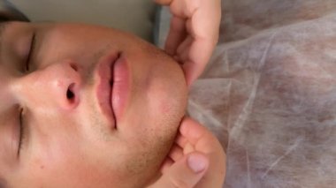 El terapisti genç adam için yüz masajı yapıyor..