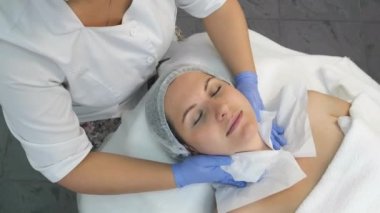 Kozmetik uzmanı işlemden önce kağıt peçete kullanarak kadınların yüzünü siliyor..