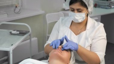 Cosmetologist is applying yellow peeling on womans face massaging movements.