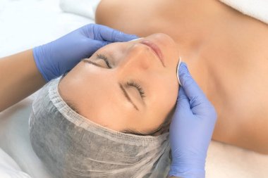 Kozmetik uzmanı kadın yüzünü siliyor. Ameliyat sonrası pamuk pedi kullanıyor..