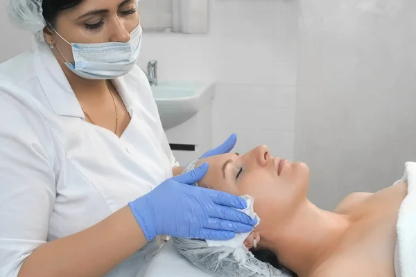 Cosmetologo sta pulendo il viso delle donne utilizzando tovaglioli prima della procedura di peeling. — Foto Stock