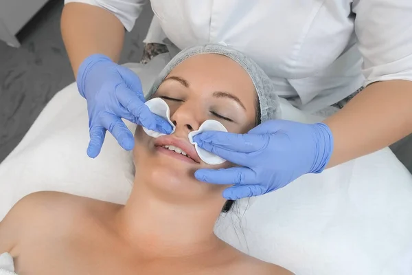 Cosmetologist wiping womans face using cotton pads before peeling procedure.