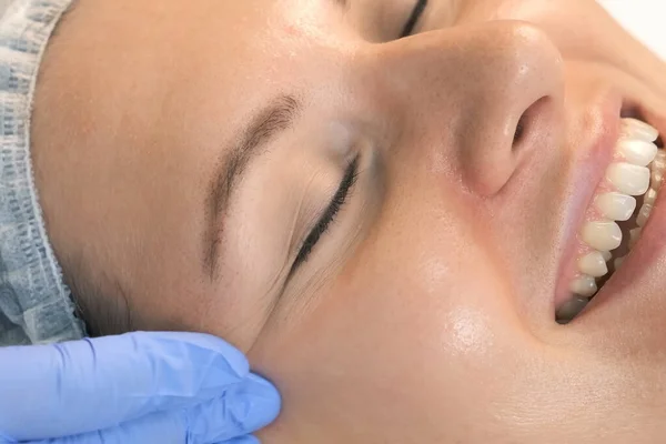 Косметолог наносит желтую пилинг на лицо женщины в клинике красоты. — стоковое фото