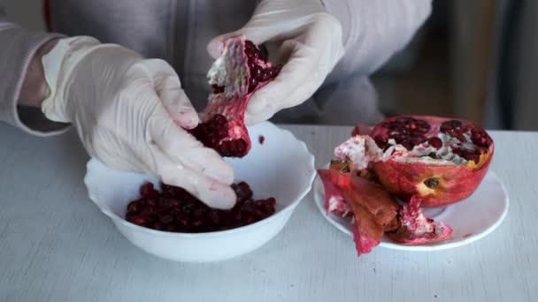 Kvinna i handskar skalar ett granatäpple över plattan på bordet, händer närbild. — Stockvideo