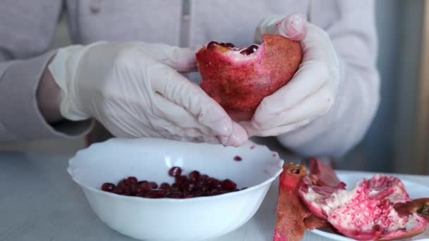 Tangan womans dalam sarung tangan mengupas membersihkan buah delima di atas piring di atas meja. — Stok Video