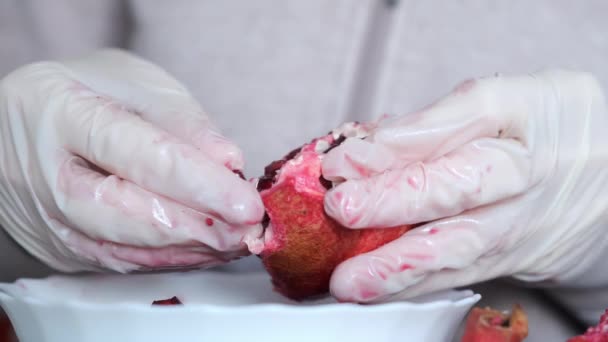 Vrouwen handen in handschoenen schillen het reinigen van een granaatappel over de plaat op tafel. — Stockvideo