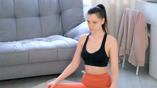 Giovane donna sta facendo esercizio di yoga per il collo seduto sul tappeto a casa. — Video Stock