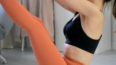 Kadın yoga yapıyor, Navasana tekne pozu veriyor. Halıda oturuyor, yandan bakıyor..