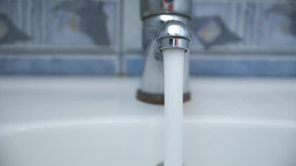 Clear water is pouring from shiny faucel into the sink in bathroom, closeup. — Stock Video