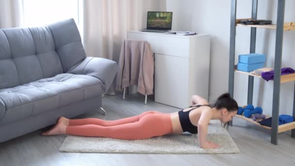 Молода жінка робить вправи з колін вдома на килимі, вид збоку . — стокове відео