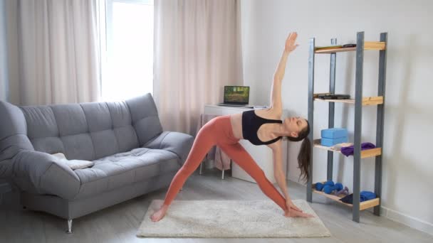 Fiatal nő gyakorolja Trikonasana Háromszög Pose jógázik otthon. — Stock videók