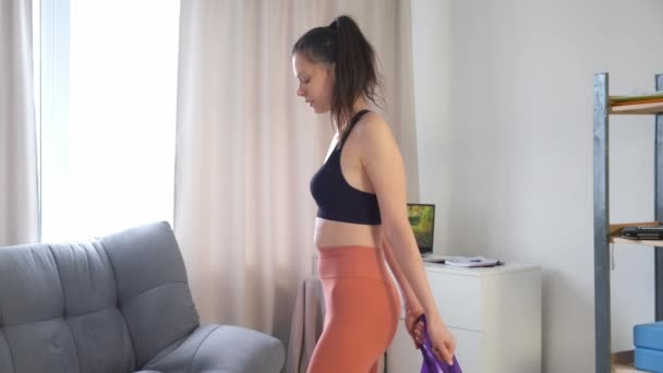 Spor giyim bölümündeki kadın evinde direnç bandıyla bacak ve sırt büküyor.. — Stok video
