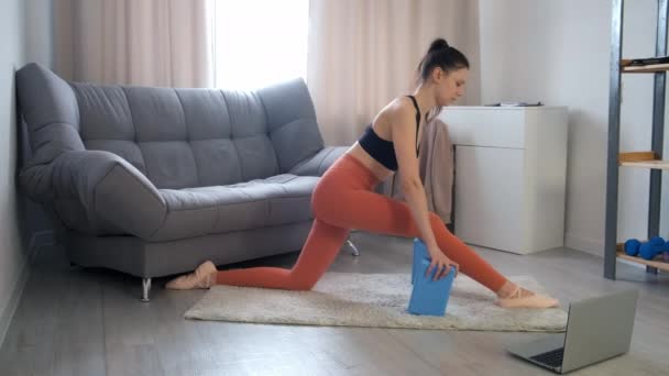 Mujer joven deportiva flexible haciendo división longitudinal sentado en la alfombra en casa. — Vídeo de stock