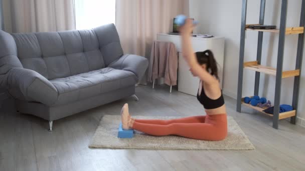 Mujer joven está practicando yoga haciendo inclinaciones en pose de flexión sentada hacia adelante en casa. — Vídeo de stock