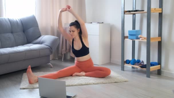 Woman is doing stretching tilts to leg exercise at home looking on laptop. — Vídeo de Stock