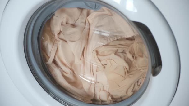 Máquina de lavar roupa com roupa de cama bege no interior está funcionando, lavanderia em casa. — Vídeo de Stock