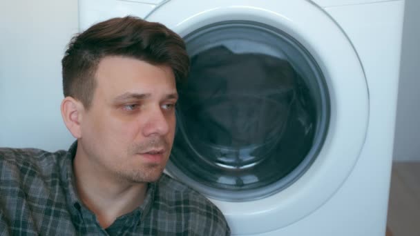 Moe man wacht op de wasmachine met grijze sprei erin. — Stockvideo